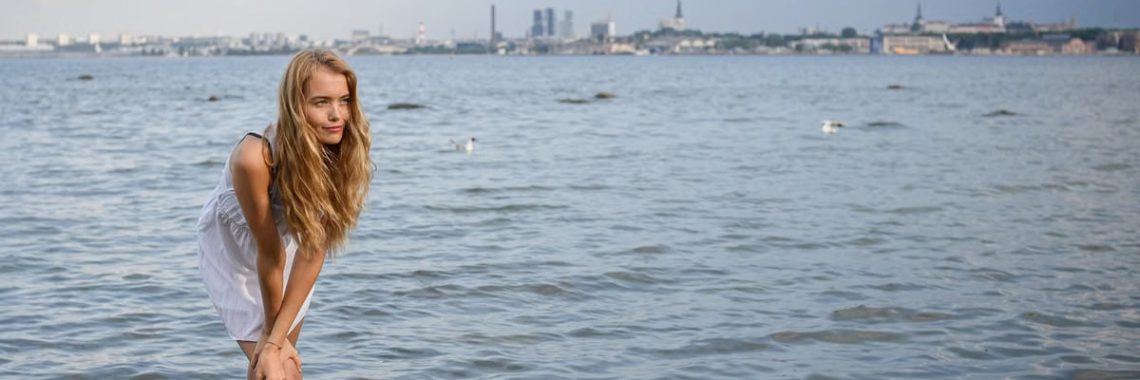Young woman standing in water with Tallinn skyline in the background on a sunny day.